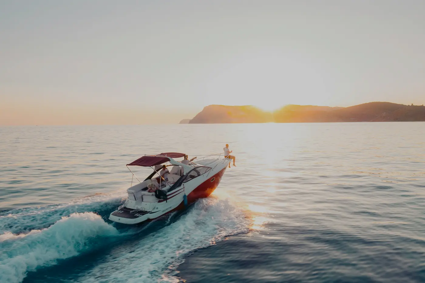 Motorboat cutting across calm water at sunrise