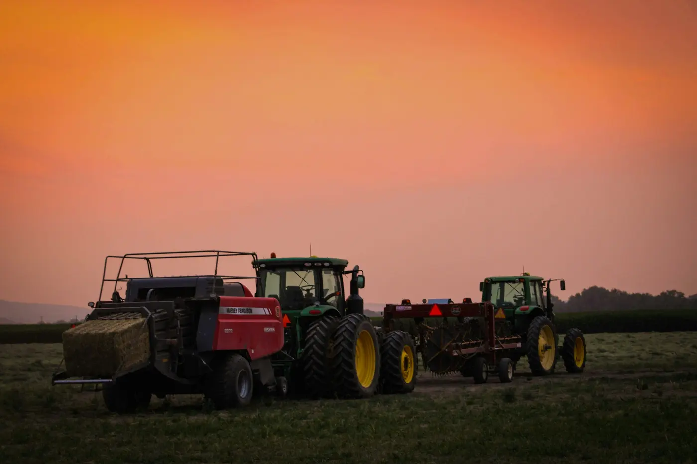 Farm tractors and equipment parked in a field under an orange sky