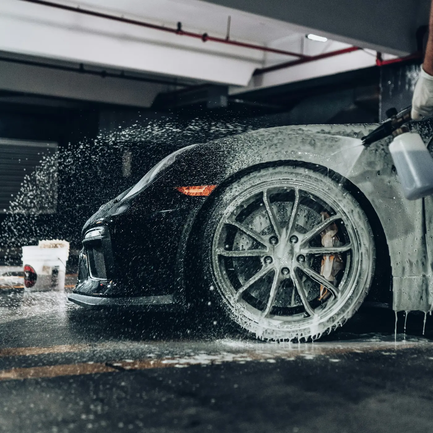 Black sports car wheel covered in soap foam during a wash