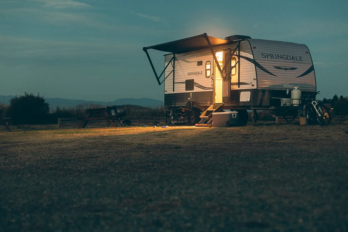 Travel trailer parked in a field at dusk with its interior lights glowing