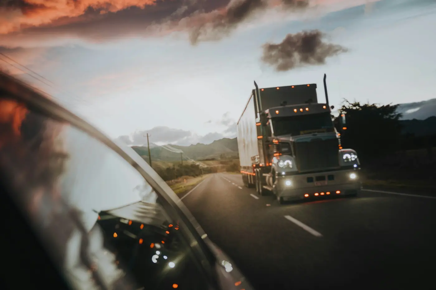 Semi truck driving down a highway at dusk under a warm orange sky
