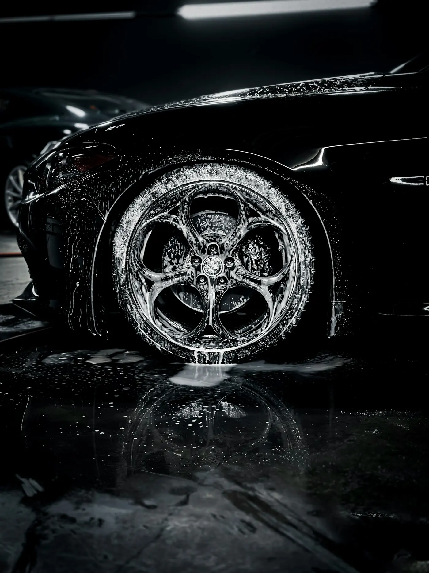 Wet black wheel with foam and reflections on a glossy floor