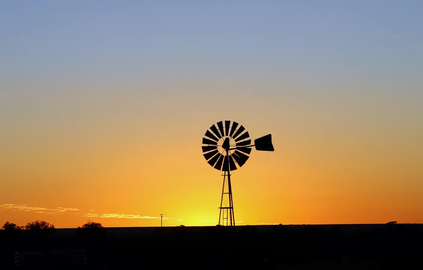 Farm windmill silhouetted against an orange sunset